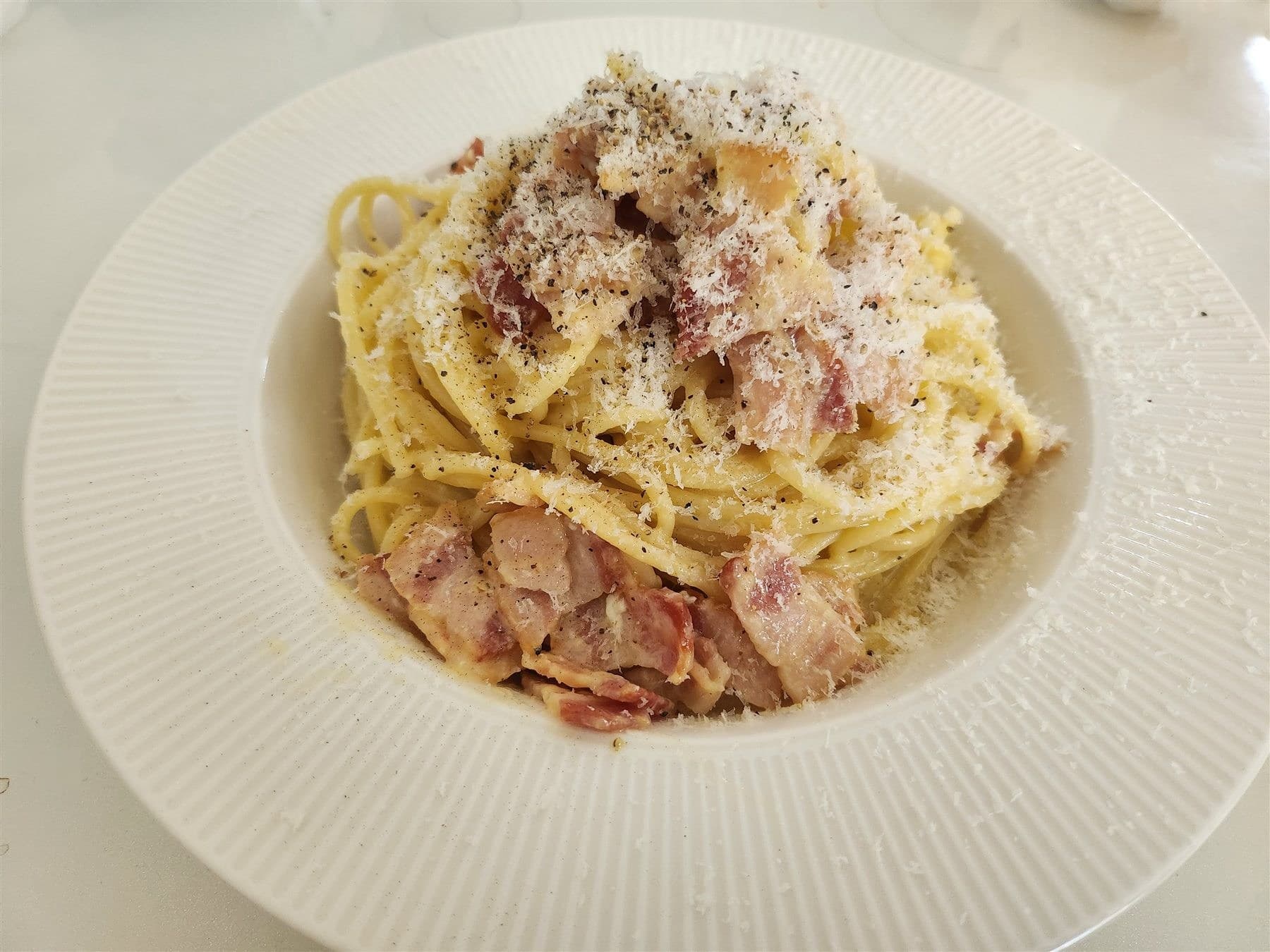 A bowl of spaghetti carbonara topped with black pepper and grated cheese.