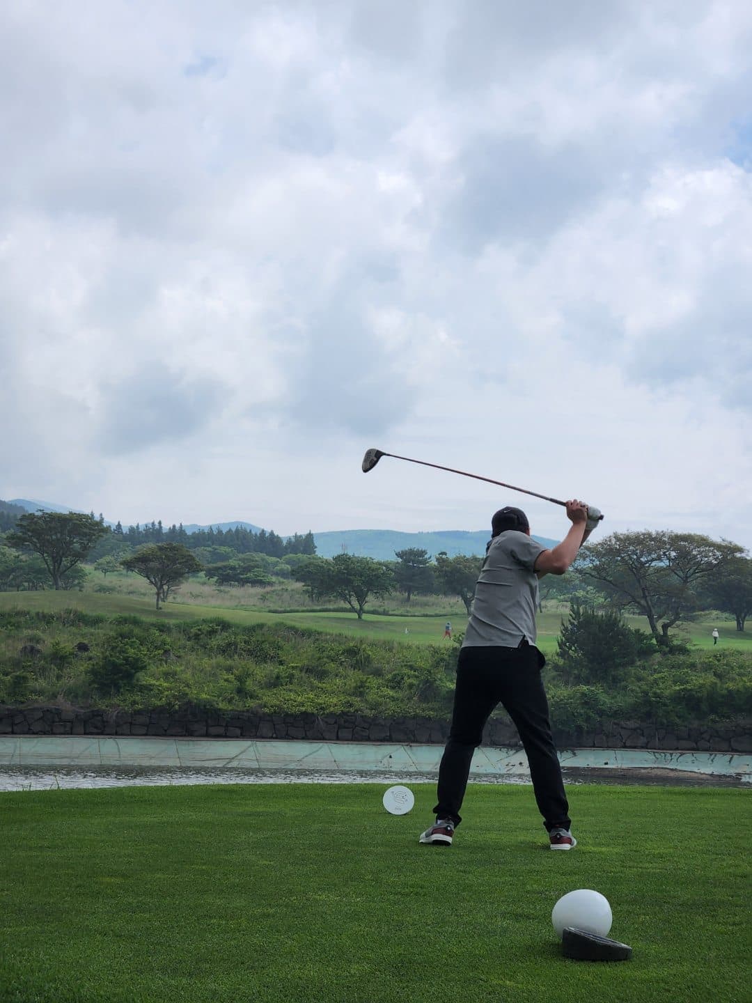 A golfer following through on a swing at a course overlooking hills and a water hazard.
